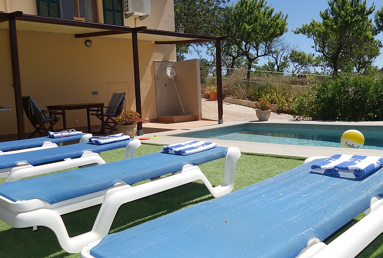 Finca Poolbereich Sonnenliegen Tisch Stuehle Baeume